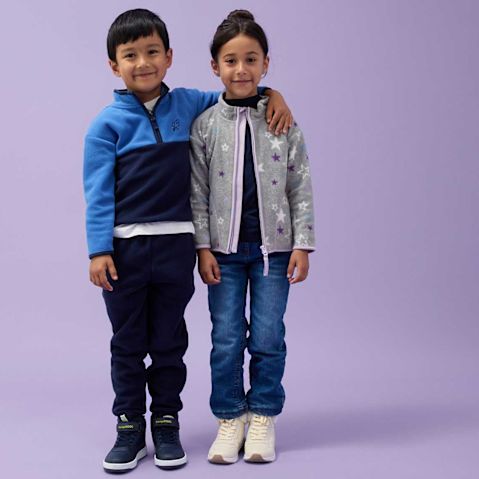 Kinder in Jeans und Jacken: blaue Jacke für ihn, graue Jacke für sie.