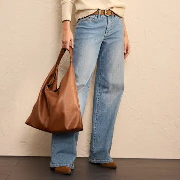Lässiger Look mit weiter Jeans, cremefarbenem Pullover und brauner Ledertasche.