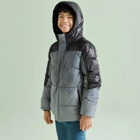 Das Kind trägt eine modische zweifarbige Steppjacke in Grau und Schwarz, dazu Jeans.