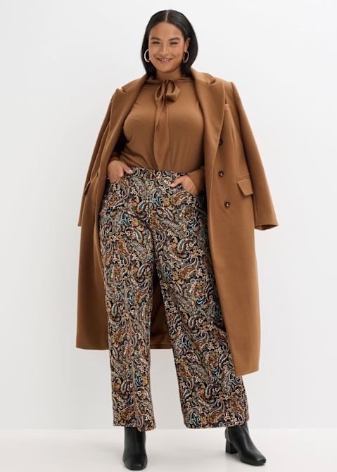 Camelmantel über gemusterter Hose und farblich abgestimmter Bluse mit Schleifenkragen.