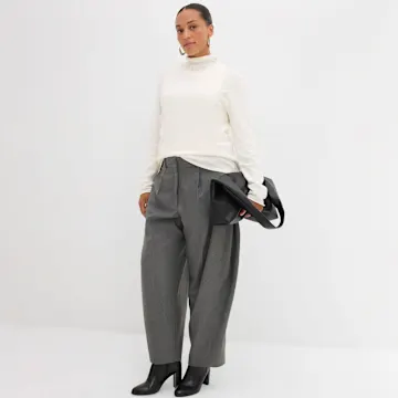Cremefarbener Rollkragenpullover kombiniert mit weiten grauen Hosen und schwarzen Stiefeln.