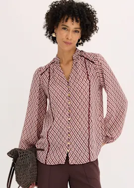 Modische Bluse mit Rautenmuster, langen Ärmeln und kontrastierenden Paspeln, dazu dunkle Hose.