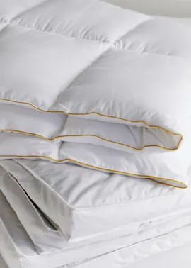 Weiche, weiße Bettdecken und Kissen mit feinen goldenen Rändern laden zum Kuscheln ein.
