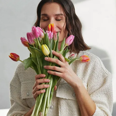 Ein weißer, kuscheliger Pullover umhüllt sanft die Person, die bunte Tulpen hält.