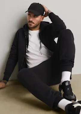 Schwarze Kappe, Kapuzenjacke, weißes T-Shirt, Jogginghose, weiße Socken und Turnschuhe.