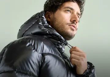 Der Mann trägt eine stylische, glänzende schwarze Daunenjacke mit Kapuze.