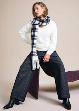 Flauschiger weißer Pullover, karierter Schal, weite dunkle Hose und stylische Stiefeletten.