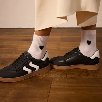 Schwarze Sneaker mit weißen Streifen und weiße Socken mit Herzchen.