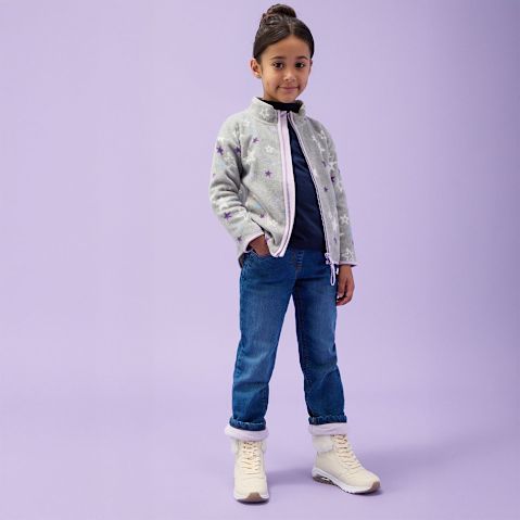 Gemusterte Jacke, dunkles Shirt und Jeans kombiniert mit weißen Stiefeln.