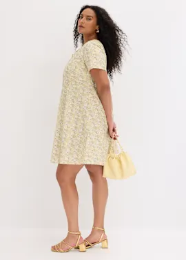 Ein leichtes gelbes Blumenkleid, goldene Riemchensandalen und eine gelbe Beuteltasche.