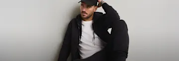 Mann trägt schwarze Kappe, schwarzen Hoodie und weißes T-Shirt.