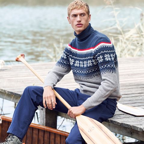 Ein Mann in einem gemusterten Norwegerpullover und Jeans sitzt entspannt auf einem Boot.