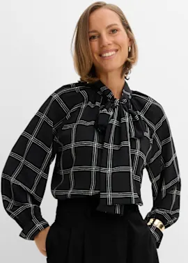 Elegante schwarze Bluse mit Karomuster und Schleife, schwarze Hose, goldener Armreif.