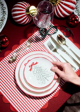 Weihnachtlich gedeckter Tisch: rote Tischdecke, gestreiftes Set, Teller, Besteck und Kugeln.