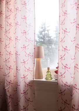 Rosa Vorhänge mit Schleifenmuster schmücken das Fenster zusammen mit Lampe und Kerze.