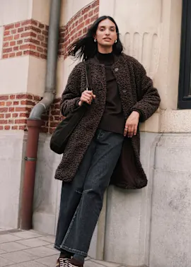 Brauner Teddymantel, Rollkragenpullover, dunkle Jeans und Sneaker bilden ein stilvolles Outfit.