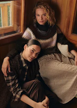 Kuschelige Mode mit Strickpullover, kariertem Rock, kariertem Hemd, Weste und brauner Hose.