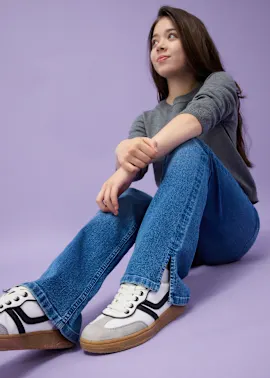 Lässiger Look mit grauem Shirt, Jeans mit Schlitz und weißen Sneakers.