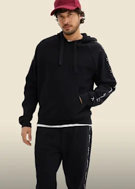 Lässiger schwarzer Hoodie und Jogginghose mit Schriftzügen, dazu rote Kappe.