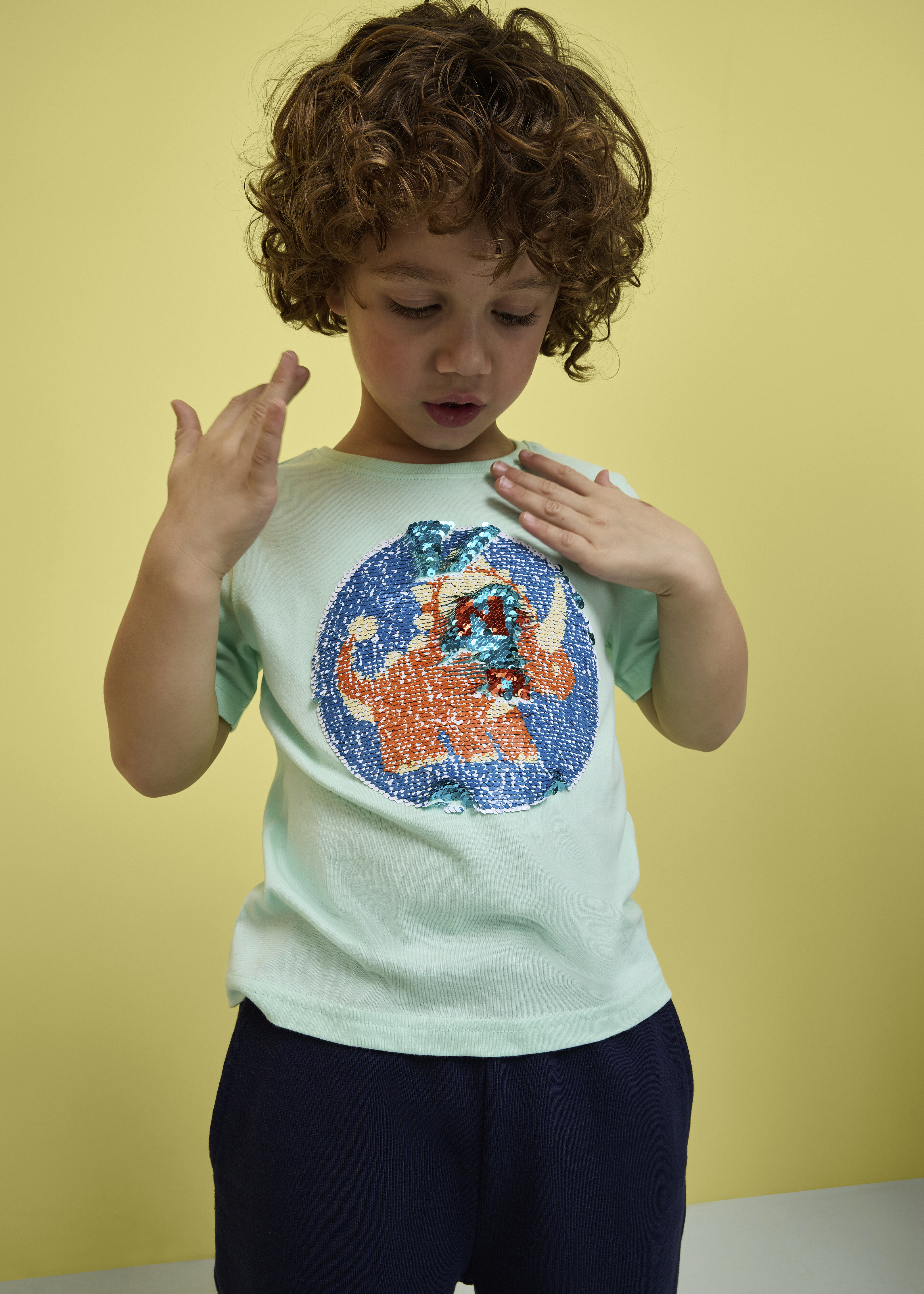 Kind trägt ein türkises T-Shirt mit buntem Aufdruck.