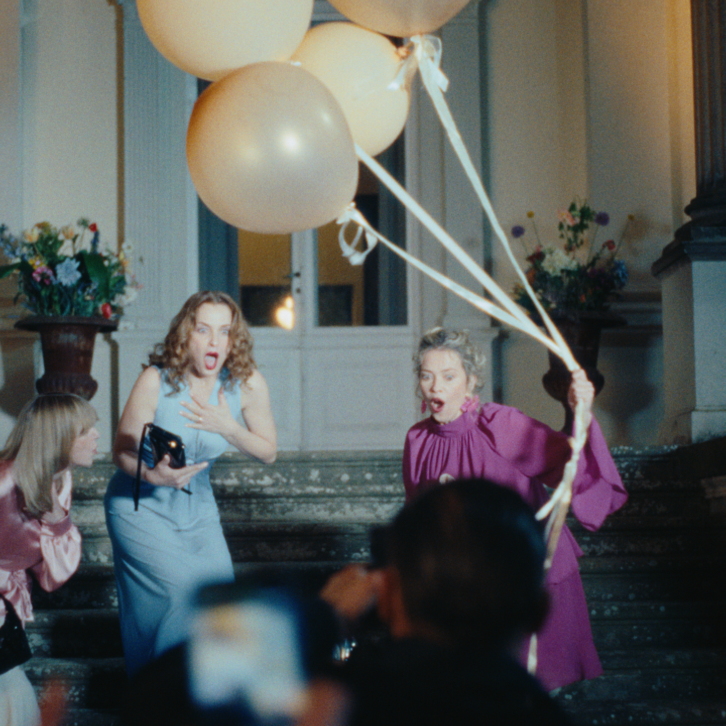Zwei Frauen schauen überrascht und die eine hält Luftballons fest.