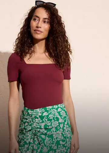 Burgunderrotes Shirt kombiniert zum grün-weißer Blumenrock.