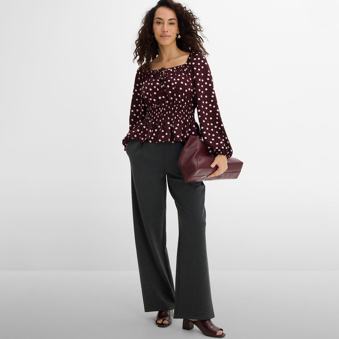 Gepunktete Bluse, weite graue Hose und bordeauxrote Accessoires.