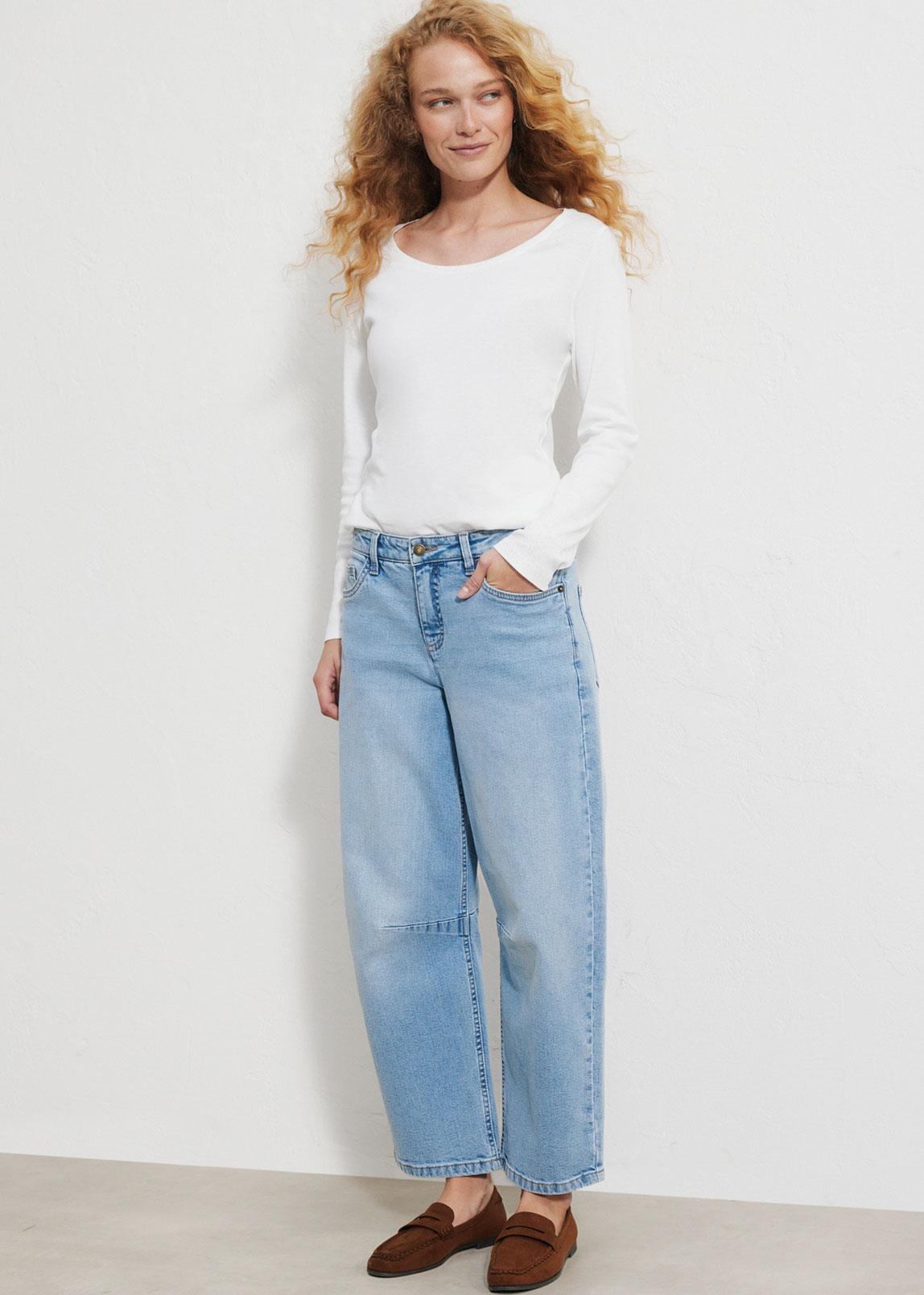Weißes Langarmshirt, weite blaue Jeans und braune Loafer.