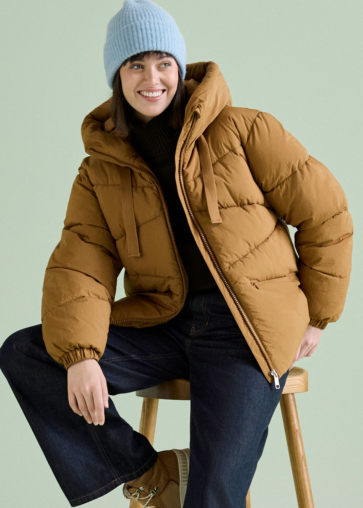 Die Frau trägt eine braune Steppjacke, blaue Mütze und dunkle Jeans.