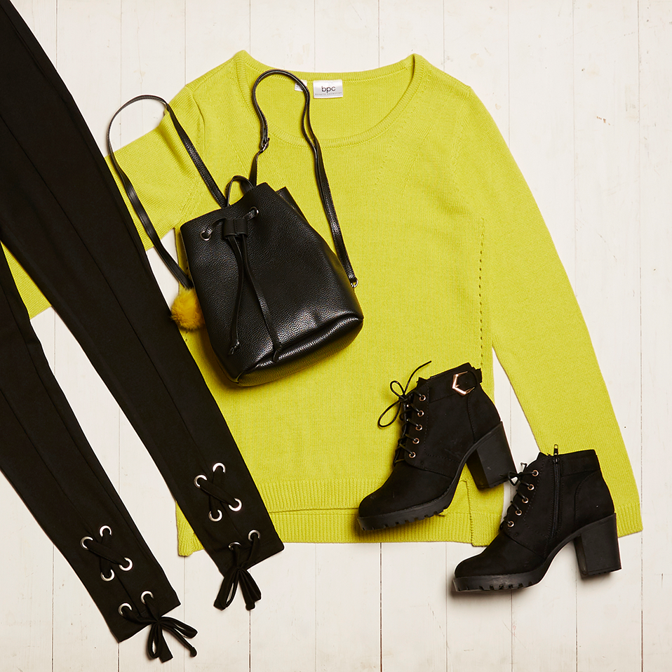 Leuchtend gelber Pullover kombiniert mit schwarzen Accessoires: Stiefeletten, Gürtel und Beuteltasche.