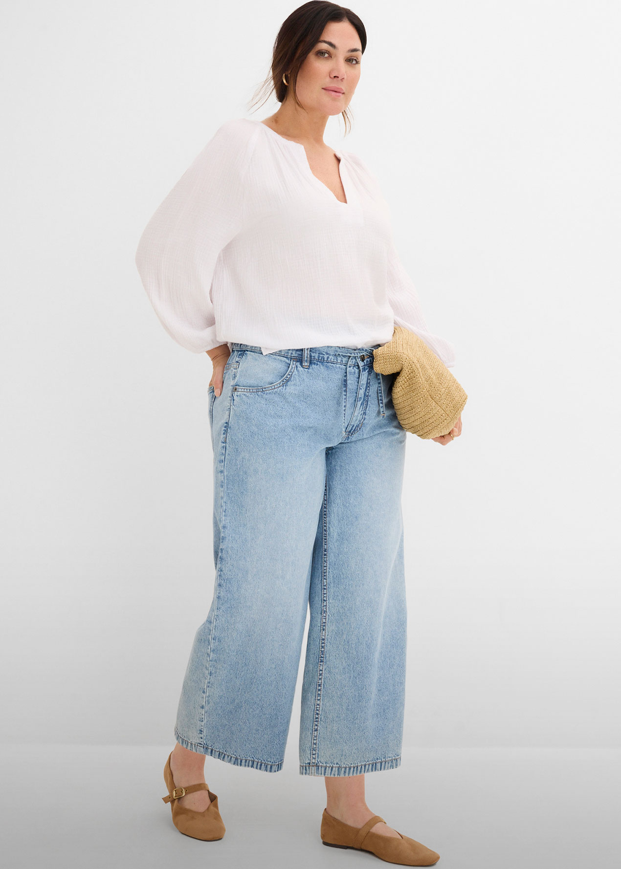 Lockere weiße Bluse, weite Jeans, dazu braune Schuhe und Flechttasche.