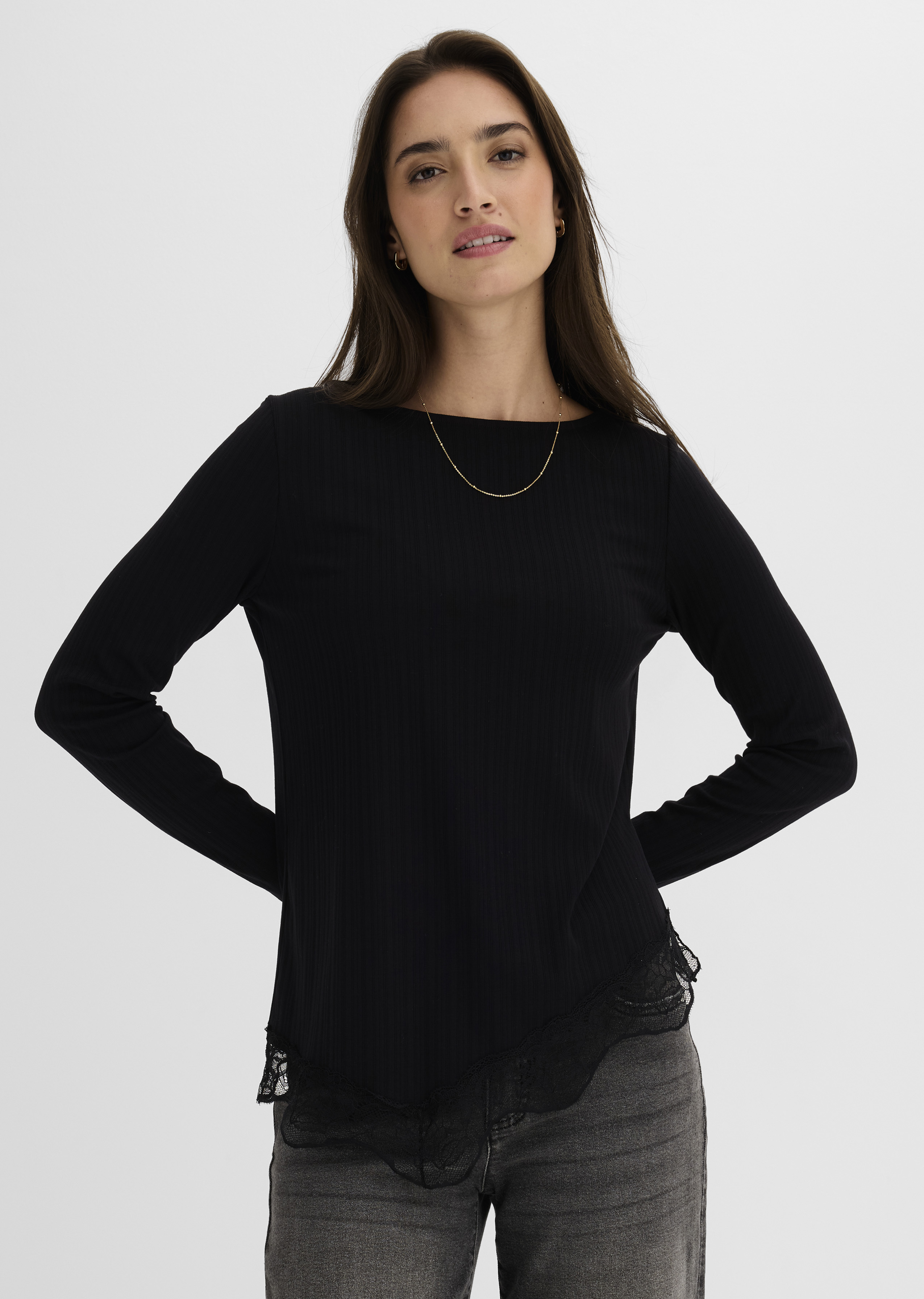 Schwarzes Ripp-Langarmshirt mit elegantem Spitzenbesatz, kombiniert mit lässiger grauer Jeans.