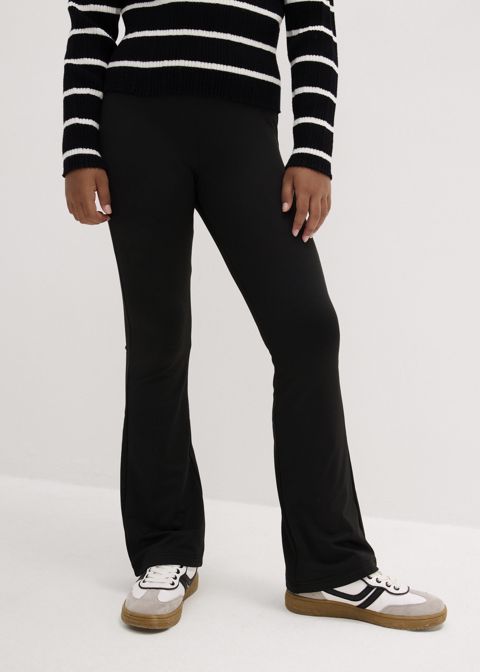 Rosafarbenes Oberteil, schwarze weite Hose mit Bindeband und sportliche Sneaker.