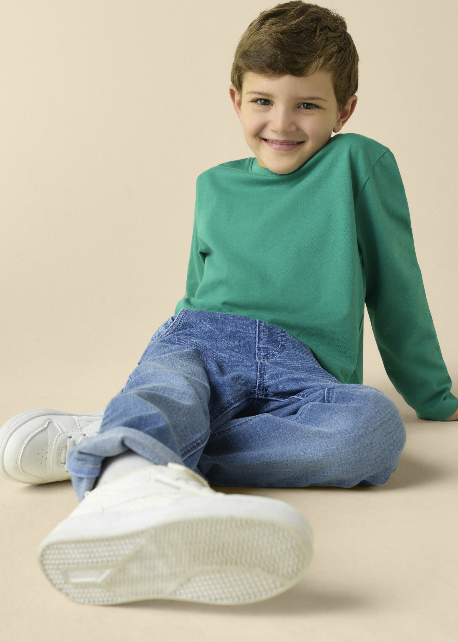 Grünes Langarmshirt, blaue Jeans und weiße Sneaker – ein bequemes Outfit für Kinder.
