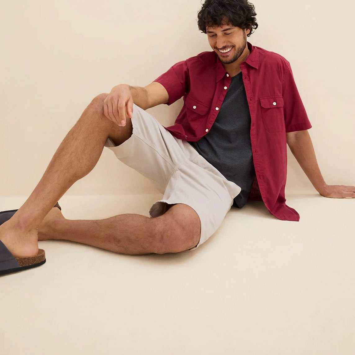 Rotes Kurzarmhemd über dunklem Shirt, dazu helle Shorts und bequeme Sandalen.