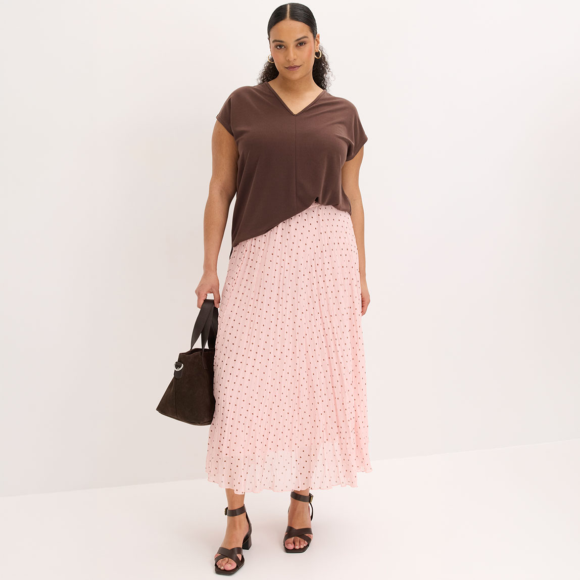 Braunes V-Shirt, rosa gepunkteter Plisseerock und Absatzsandalen.