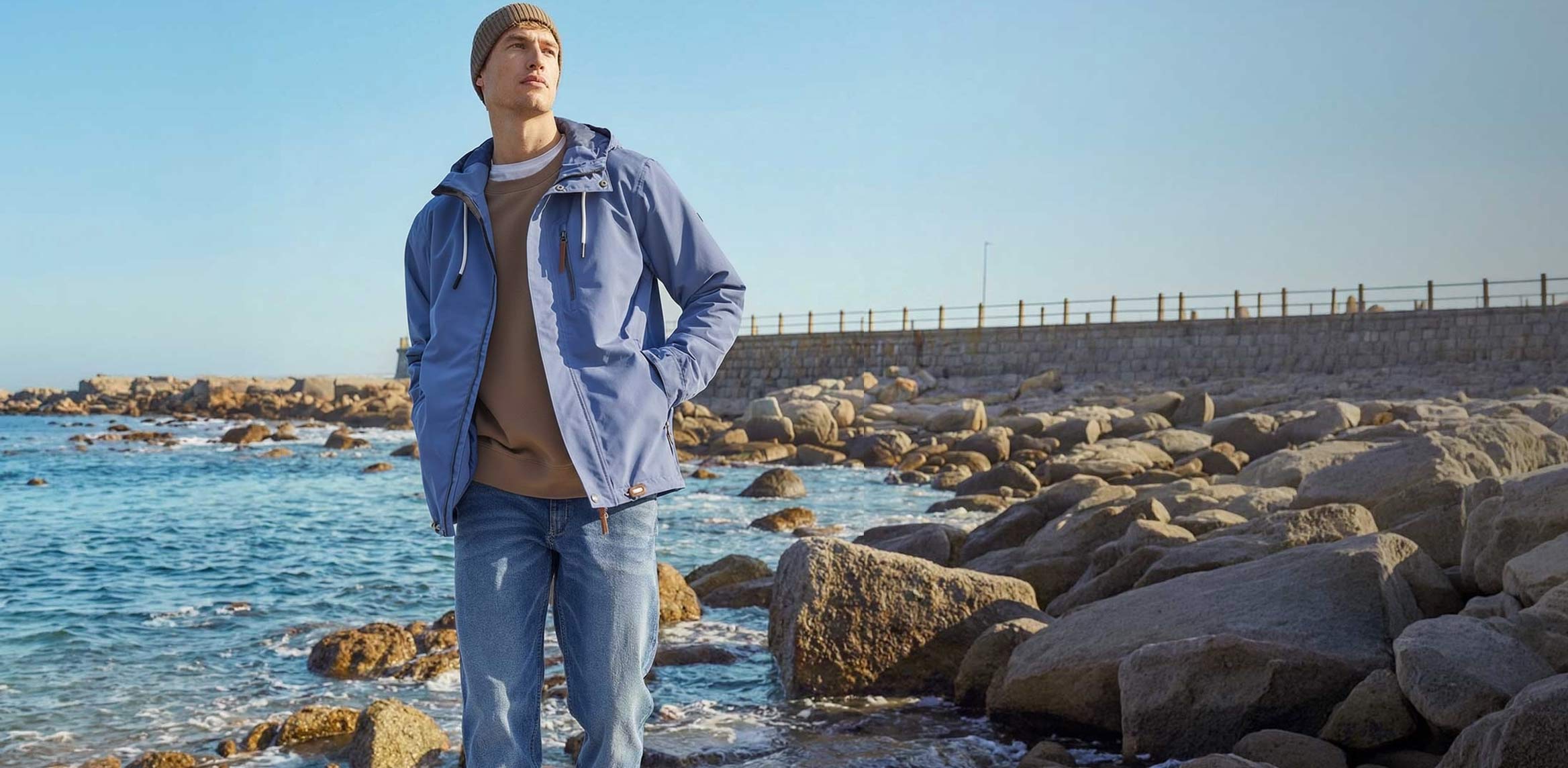 Stilvolle blaue Funktionsjacke und helle Jeans am Strand. 