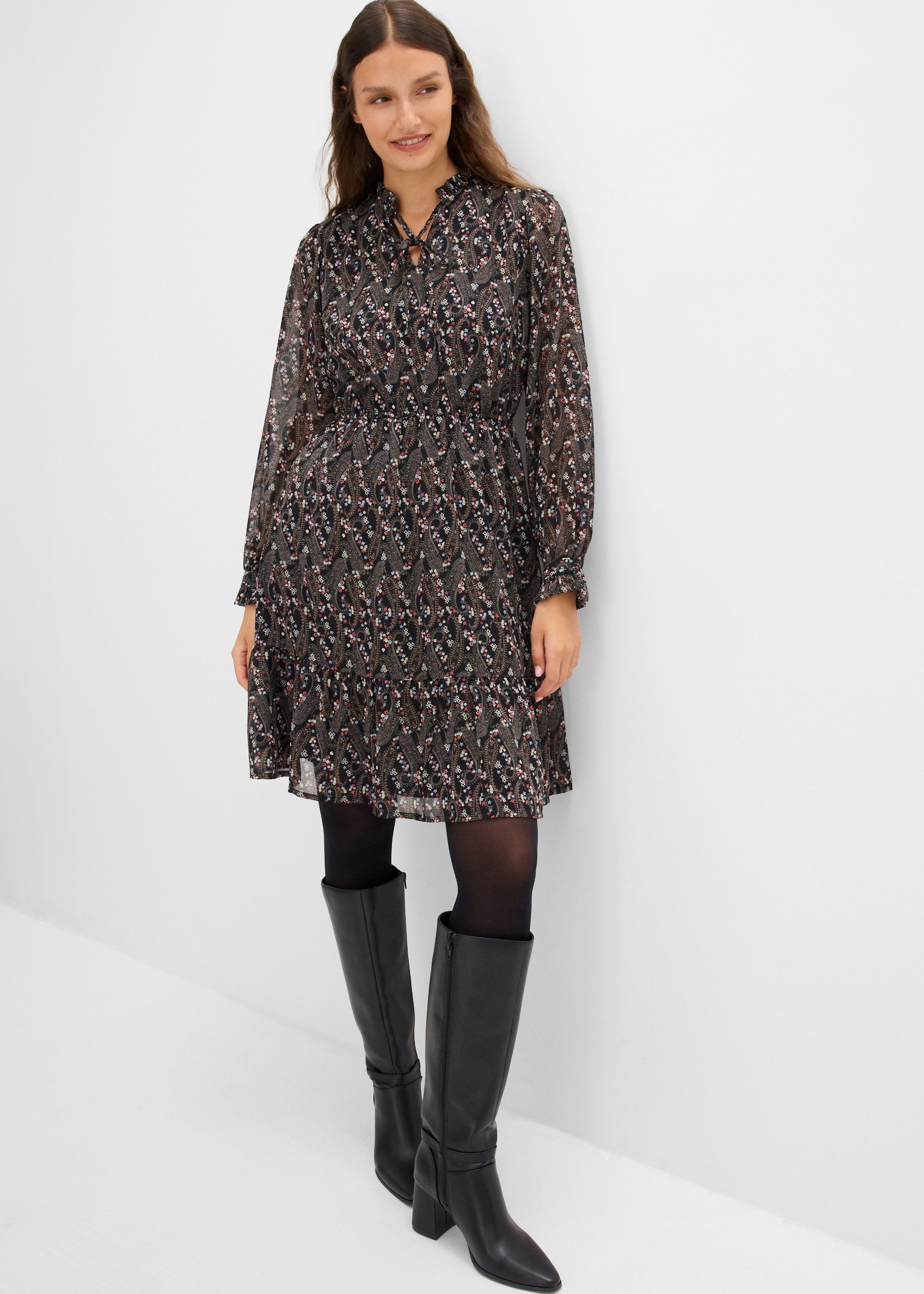 Modisches Kleid mit Muster, dazu schwarze Strumpfhose und kniehohe Stiefel.