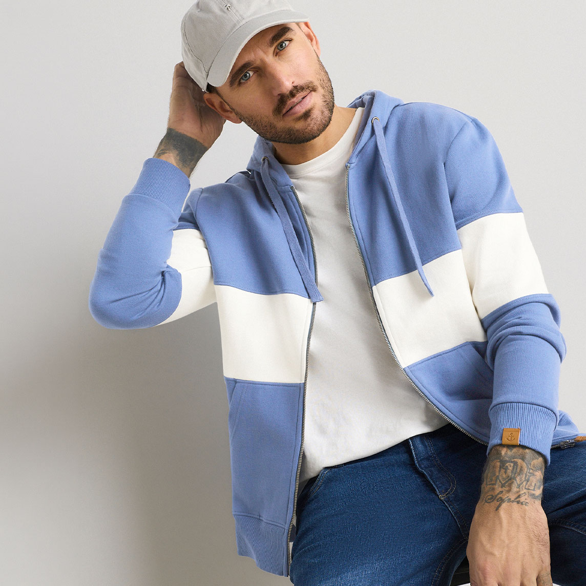 Lässiger Look: Blauer Hoodie, weißes Shirt, Jeans und graue Cap.