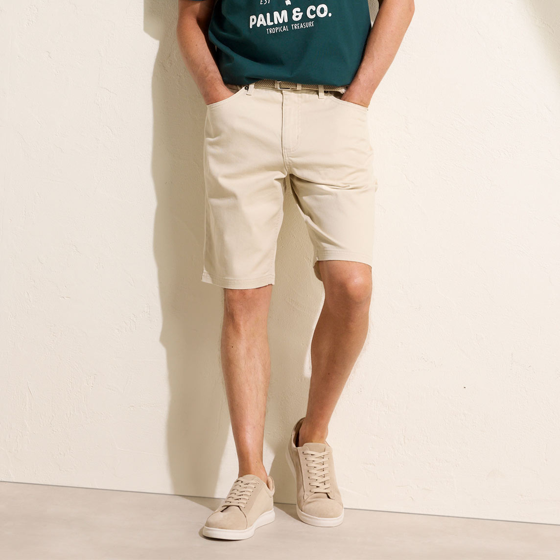 Grünes T-Shirt mit Aufdruck, beige Chino-Shorts und helle Sneaker.