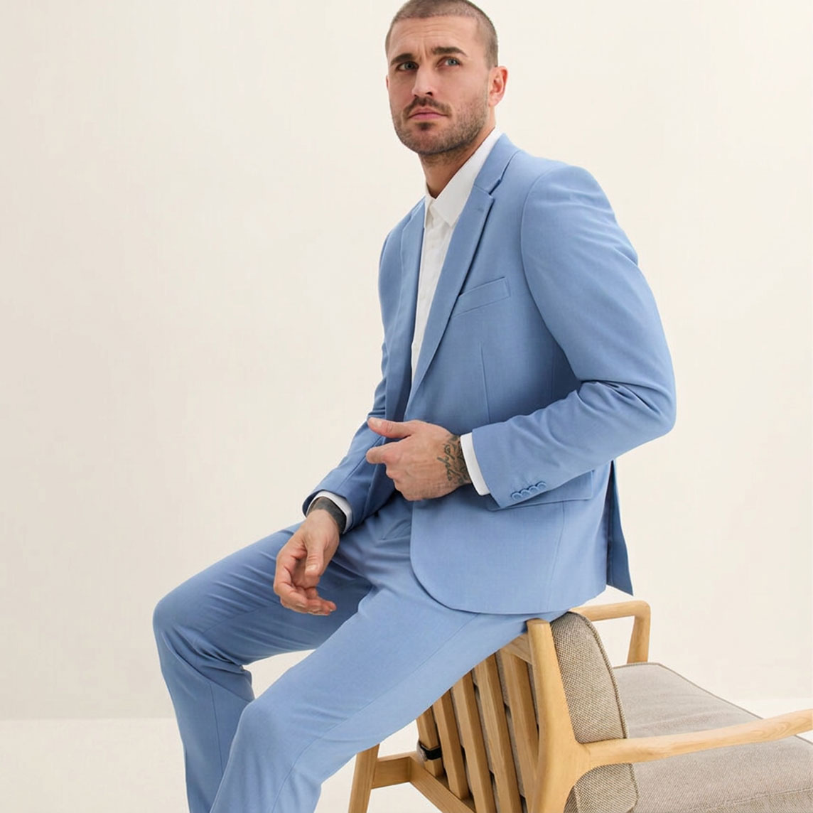 Er trägt einen eleganten, hellblauen Anzug über einem frischen weißen Hemd.