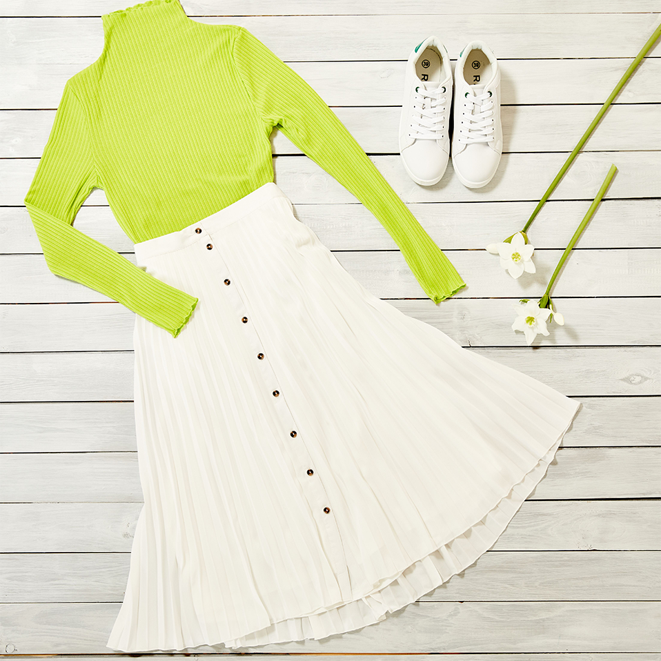 Neongrüner Pullover trifft auf weißes Sommerkleid. Sportliche Sneaker runden den frischen Look ab.