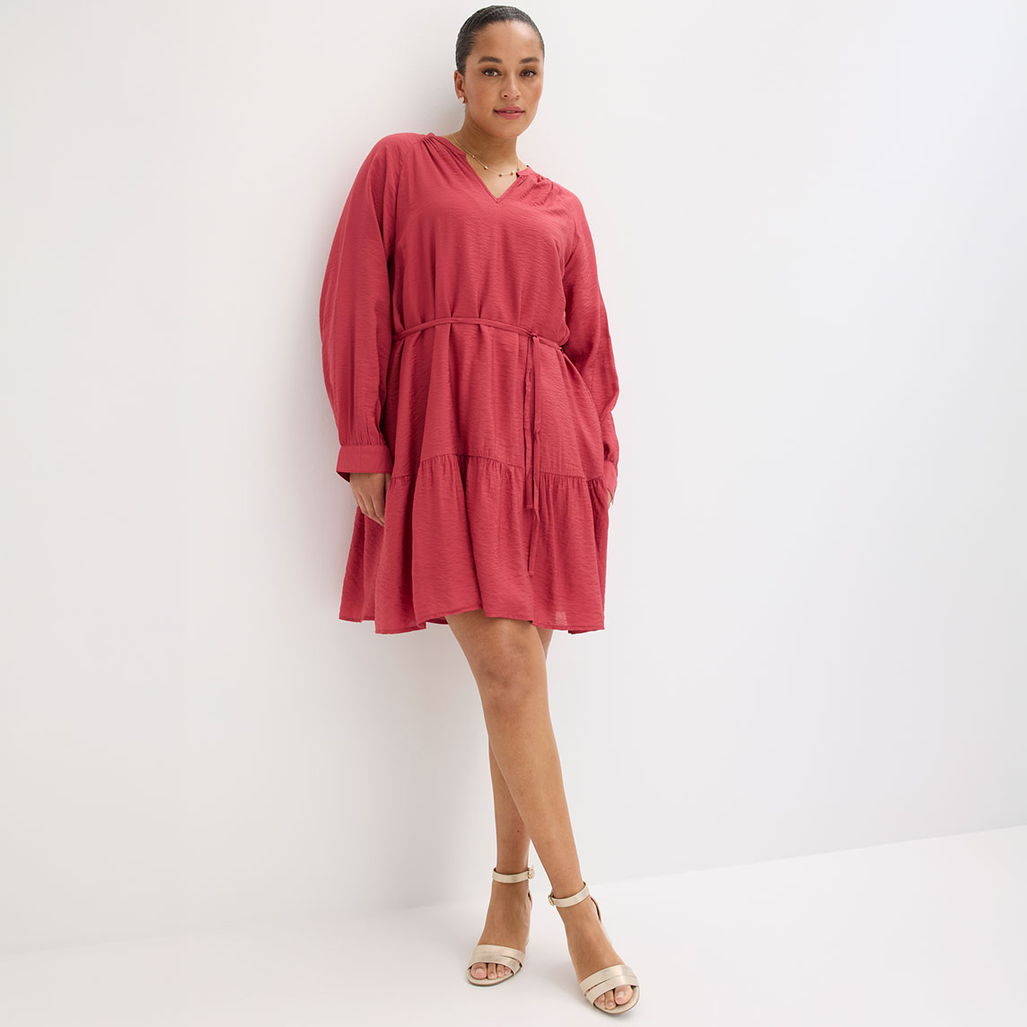Elegantes rotes Kleid mit langen Ärmeln und weißen High-Heel-Sandalen für einen stilvollen Look.
