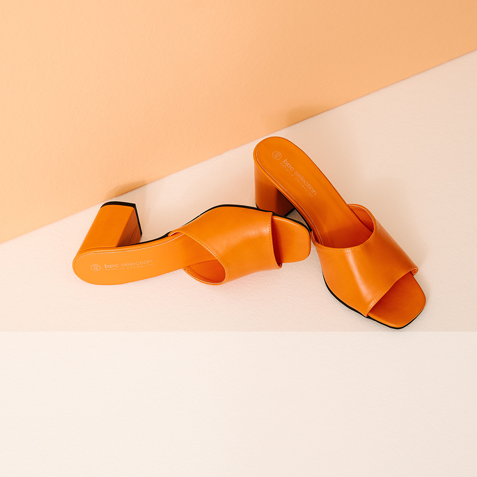 Elegante orangefarbene Ledersandalen mit offener Zehenpartie ruhen auf einer zweifarbigen Oberfläche.