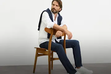 Weißes Hemd, blaue Hose, Pullover um die Schultern, weiße Sneaker.
