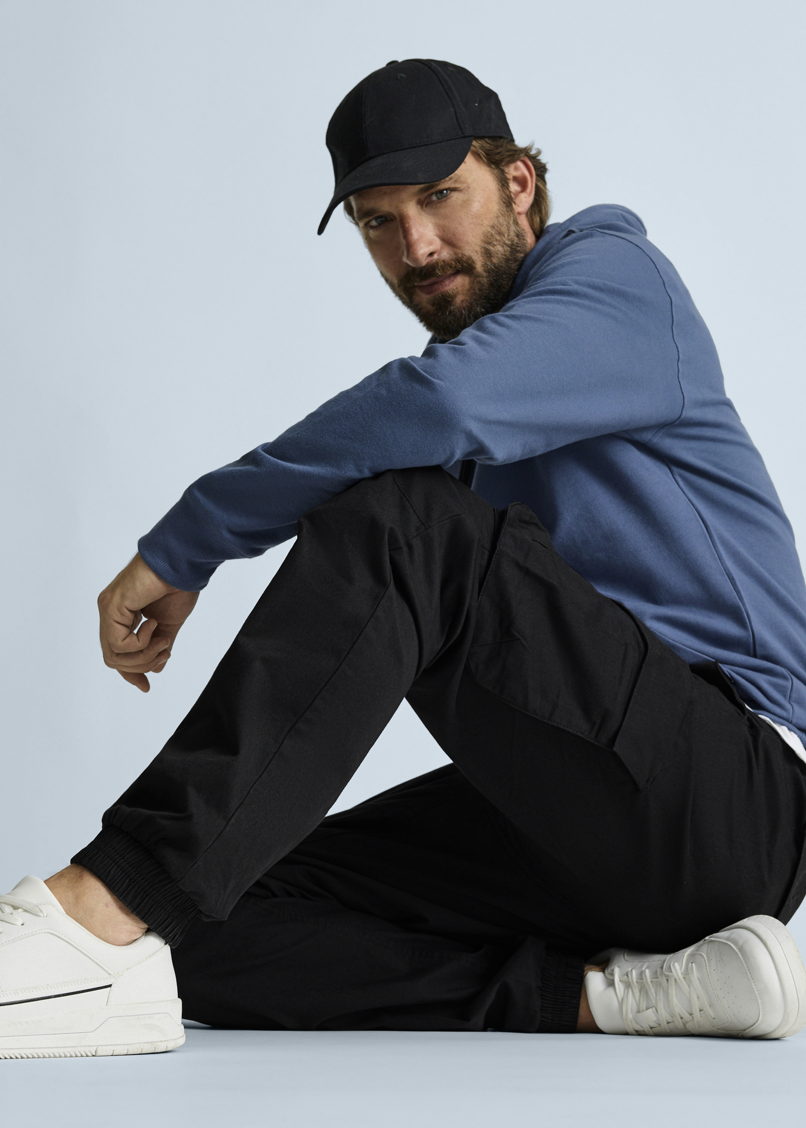 Lässiger Look: Schwarze Kappe, blauer Hoodie, bequeme schwarze Cargohose und weiße Sneaker.