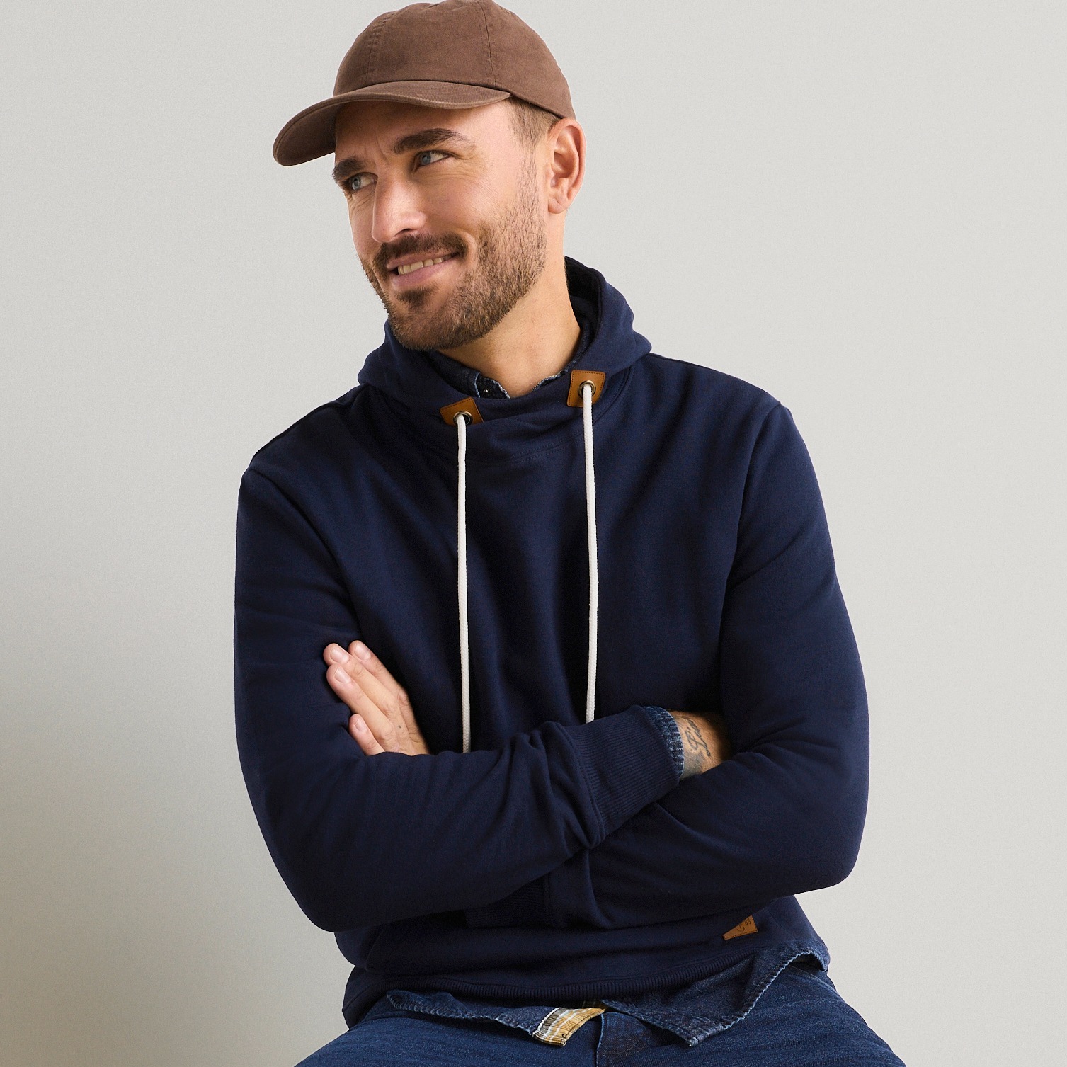 Dunkelblauer Hoodie, braune Kappe und Jeans für einen lässigen Look.