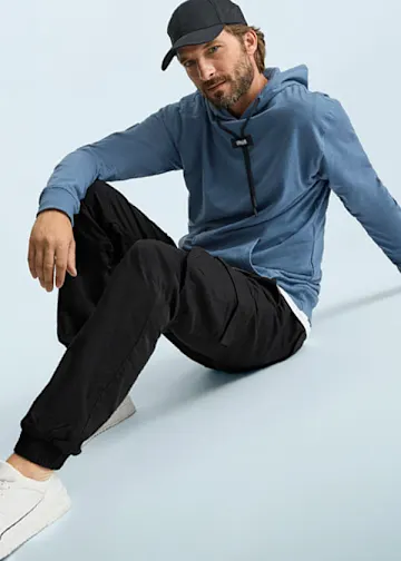 Blaue Kapuzenjacke, schwarze Cargohose, weiße Sneaker und schwarze Kappe für einen lässigen Stil.