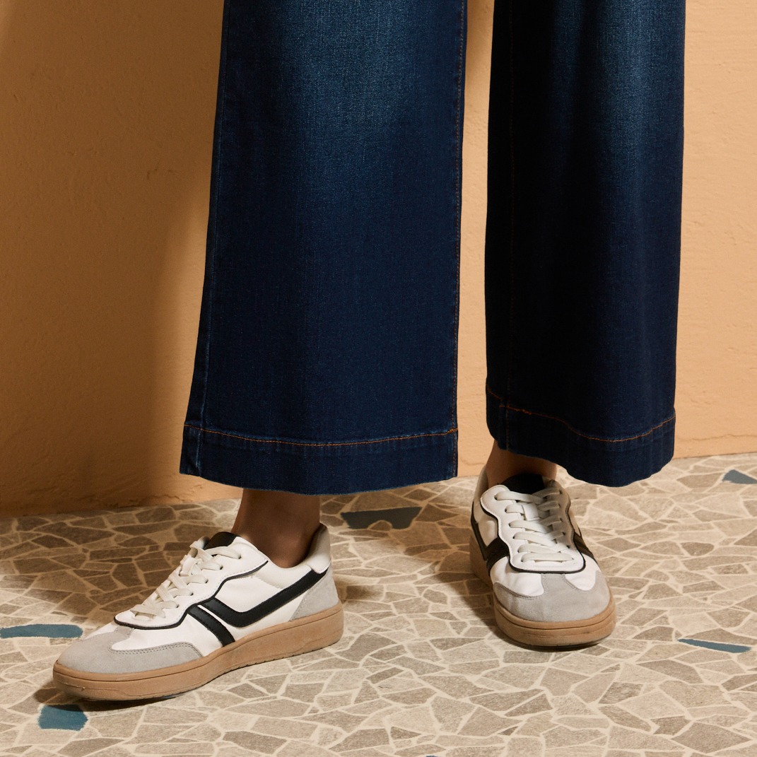 Weite Jeans in dunklem Blau, kombiniert mit klassischen Sneakers in Weiß und Schwarz.