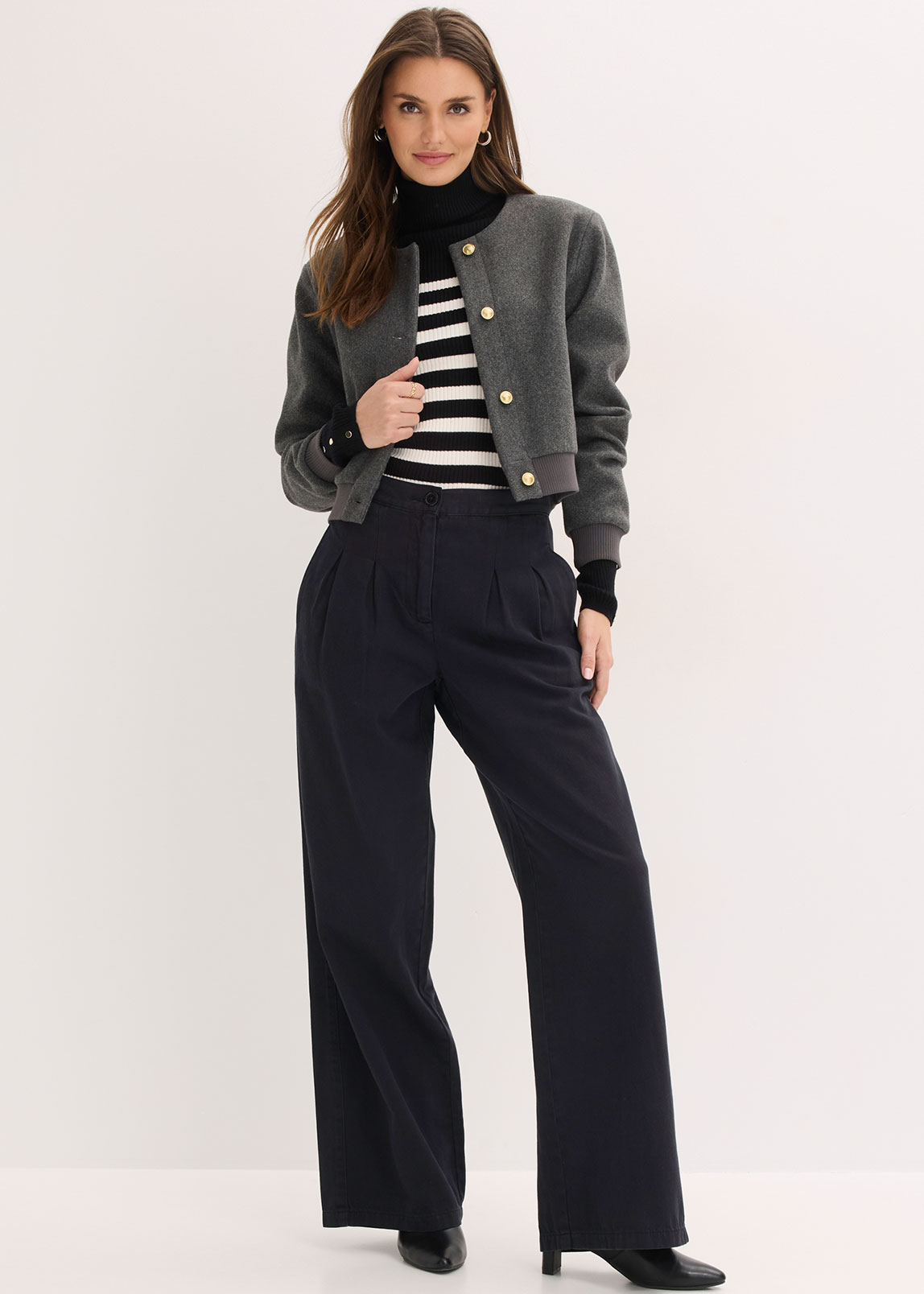 Graue Jacke, gestreifter Pullover und weite schwarze Hose.